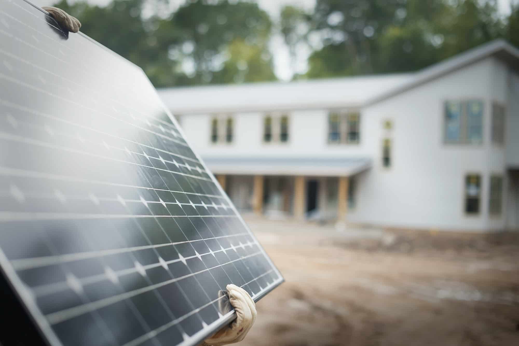 a workman carrying a large solar panel at a green house construction site